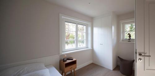 a white bedroom with a bed and two windows at Rantum Dorf - Ferienappartments im Reetdachhaus 3 & 4 in Rantum