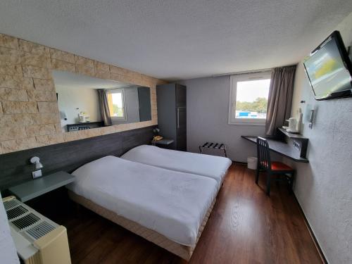 a hotel room with a bed and a desk and a television at Hôtel Restaurant Le Relais - Pau Nord in Lons