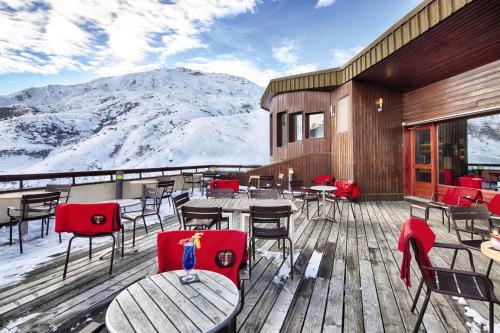 a restaurant with tables and chairs on a deck with snow covered mountains at Hôtel Les Menuires Les Bruyères in Les Menuires