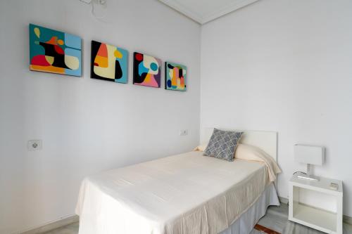 Habitación blanca con cama y pinturas en la pared en Cuna, en Sevilla