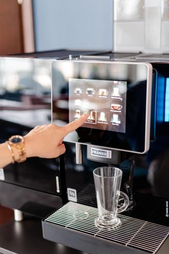 a woman is pointing at a coffee machine with a glass at Copernicus Toruń Hotel in Toruń
