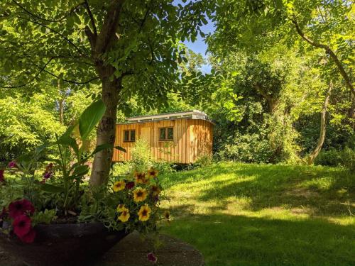 a wooden cabin in a yard with a tree and flowers at Jungle Wagon - Ecovillage Hainburg in Hainburg an der Donau