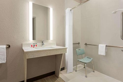a bathroom with a sink and a mirror and a chair at Days Inn & Suites by Wyndham Greater Tomball in Tomball