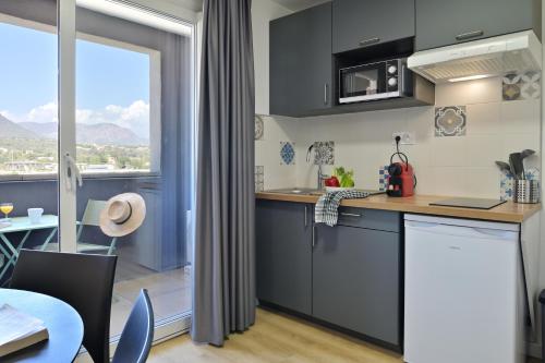 a kitchen with grey cabinets and a table and a window at Résidence Easy Lodge in Ajaccio