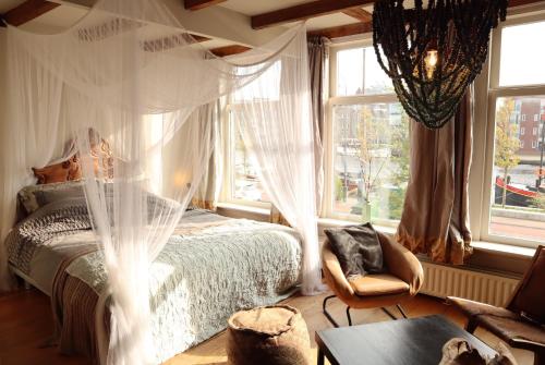 a bedroom with a canopy bed and a chair and windows at RiverSide Suite - Haarlem City Centre in Haarlem