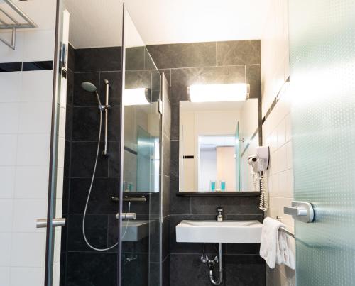 a bathroom with a shower, sink, and mirror at Bastion Hotel Groningen in Groningen