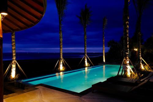 a swimming pool at night with palm trees and lights at Wide Sands Beach Retreat in Pulukan