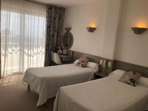 a hotel room with two beds and a window at Plage des Pins in Argelès-sur-Mer