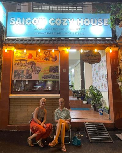 two people sitting on a bench in front of a restaurant at Saigon Cozy House & coffee in Ho Chi Minh City