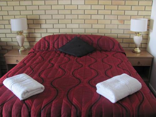 Una cama roja con dos toallas blancas encima. en Nambour Central Motel en Nambour