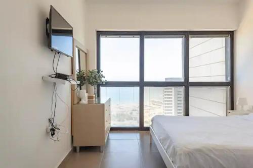 een slaapkamer met een bed en een televisie en een groot raam bij Oַ&O Group- Luxury Apt Tower Best Sea View Bat Yam in Bat Yam