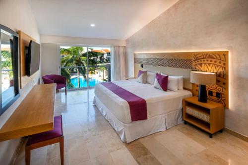 a bedroom with a bed and a desk and a television at Viva Azteca by Wyndham, A Trademark All Inclusive Resort in Playa del Carmen