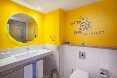 baño con paredes amarillas, lavabo y espejo en Abora Catarina by Lopesan Hotels, en Playa del Inglés