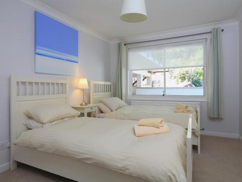 two beds in a white bedroom with a window at 2 Poundstone Court in Salcombe