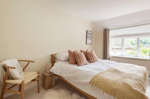 a bedroom with a bed and a chair and a window at Architect Designed Cosy Cotswold Stone Cottage in Quenington
