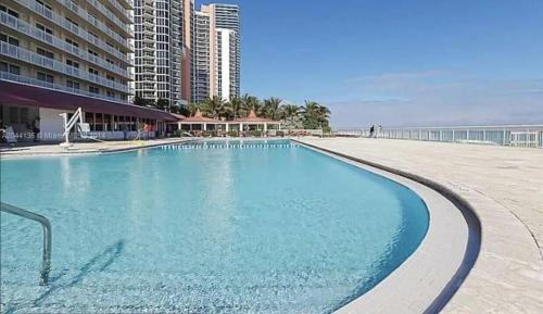 a large swimming pool next to a beach with buildings at Ramada Marco Polo Beach in Miami Beach
