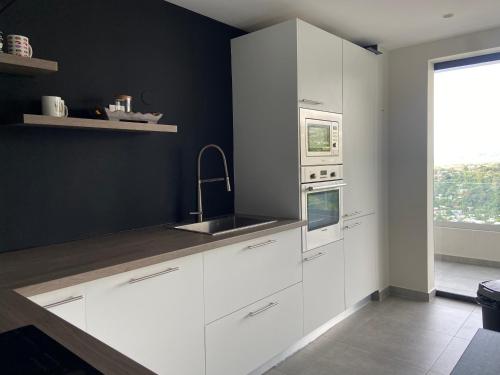 a kitchen with white cabinets and a sink and a window at Meherio - Bel Appartement vue mer à TAHITI in Papeete