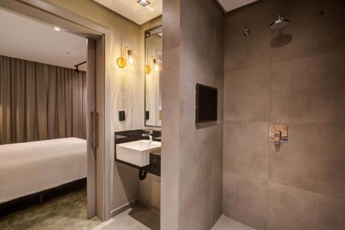 a bathroom with a sink and a bed and a mirror at Slaviero Ponta Grossa in Ponta Grossa
