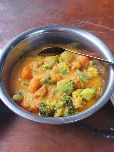 a bowl of soup with broccoli and carrots and a spoon at Sumatra Orangutan Discovery Villa in Bukit Lawang