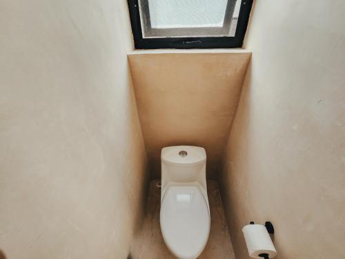 a bathroom with a toilet with a window and a toilet paper roll at Cucu Hotel El Cuyo in El Cuyo