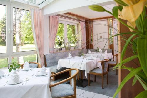 um restaurante com mesas e cadeiras brancas e janelas em Kurhotel Kaiser em Bad Wörishofen