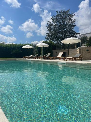 a swimming pool with blue water and umbrellas and benches at Dimorae Camà in Cisternino