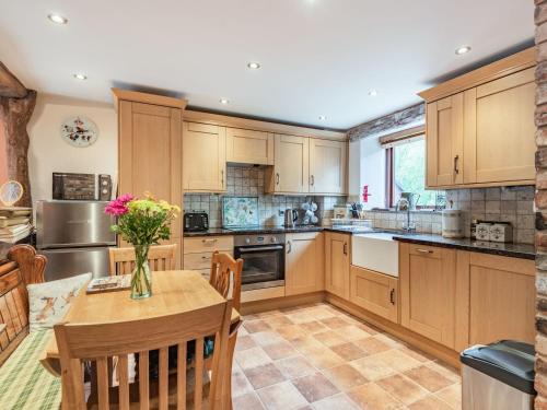 a kitchen with wooden cabinets and a table with a vase of flowers at Peacock Cottage in Dove Holes