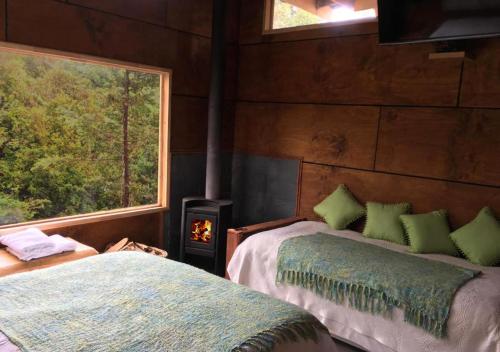 two beds in a room with a fireplace and a window at Cabañas Los Cantos del Chucao in Puerto Varas