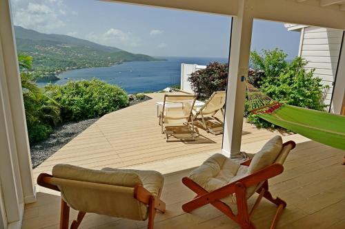 eine Veranda mit Stühlen, einer Hängematte und Meerblick in der Unterkunft LES HAUTS DE LA BAIE in Bouillante