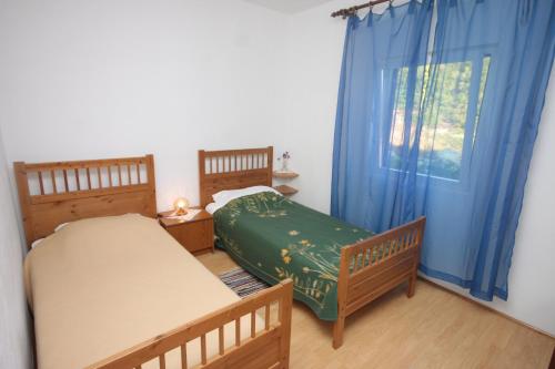 a bedroom with two beds and a window with blue curtains at Apartments by the sea Luka, Dugi otok - 8151 in Luka