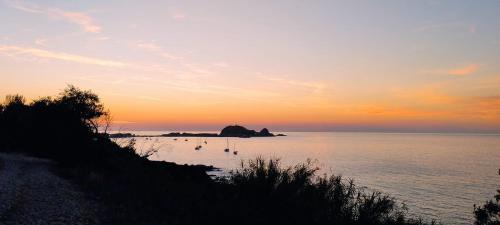 una puesta de sol sobre el océano con barcos en el agua en Maison duplex 2 chambres, avec jardin, 800m plage, en Belgodère