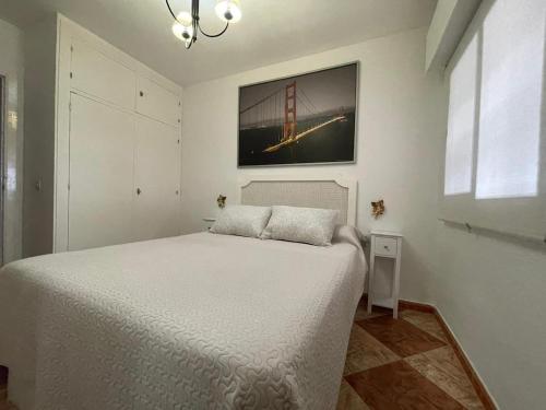 ein Schlafzimmer mit einem weißen Bett mit einem Bild an der Wand in der Unterkunft Espectacular apartamento junto al mar in Chipiona