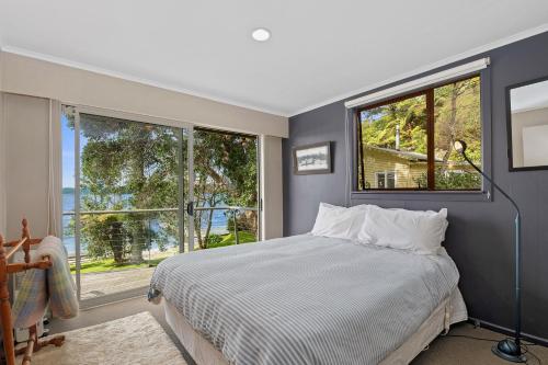 a bedroom with a bed and two large windows at Onepoto Bay Lakehouse - Lake Rotoiti Holiday Home in Okere Falls