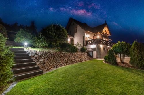 a house with a stone wall and a yard at night at Dom na wzgórzu z widokiem na jezioro z balią i sauną in Lipnica