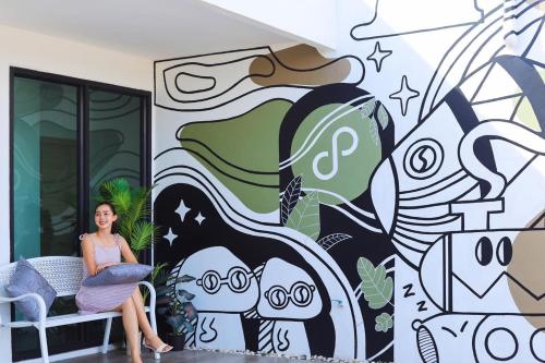 a woman sitting on a bench in front of a mural at Ananzitra Hotel in Kanchanaburi