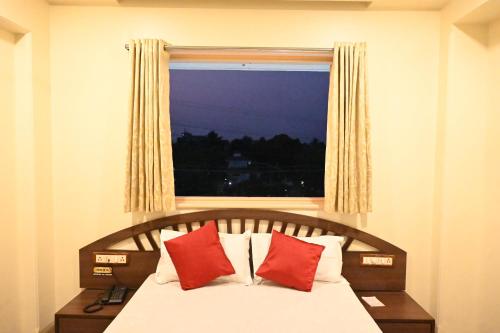 a bedroom with a bed with red pillows and a window at Hotel Sagar in Kalyan