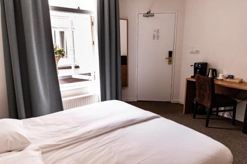 a bedroom with a bed and a desk and a window at Ambassador City Centre Hotel in Haarlem