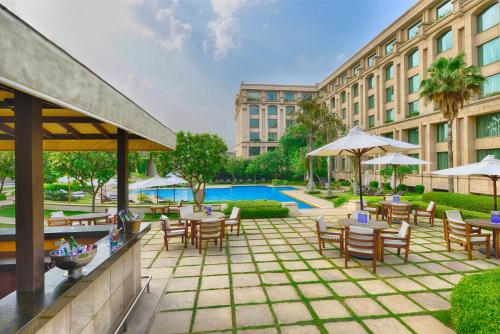 eine Hotelterrasse mit Tischen, Stühlen und einem Pool in der Unterkunft The Grand New Delhi in Neu-Delhi