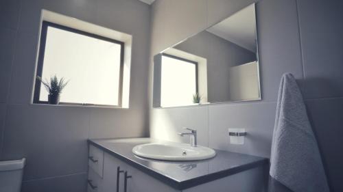 a white bathroom with a sink and two windows at Guest Suite, Lorraine Port Elizabeth in Lorraine