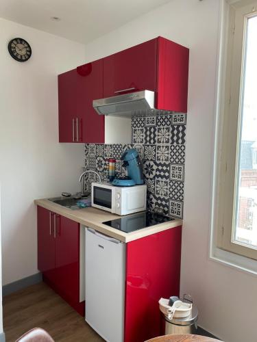 une petite cuisine avec des placards rouges et un four micro-ondes dans l'établissement 3- Au pied des Falaises du Tréport à 50m de la plage, au Tréport