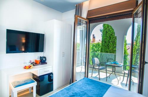a room with a bed and a television and a balcony at Acrotel Lily Ann Village in Nikiti
