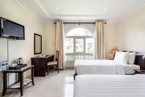 a hotel room with two beds and a desk and a television at La Bonita Hotel and Apartments in Ho Chi Minh City