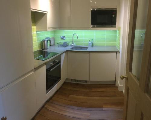 a kitchen with white cabinets and a sink and green tiles at Seaside Stay in Rustington