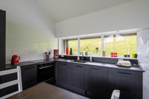 uma cozinha com armários pretos, uma janela e um lavatório em Luxurious cabin / 3 BR / Scenic village em Skálavík