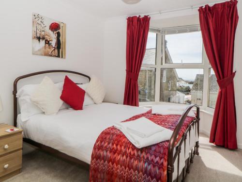 a bedroom with a bed with red curtains and a window at Meledor in Marazion