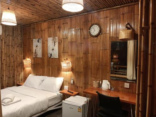 - une chambre avec un lit et un bureau avec une horloge dans l'établissement สวนเกษตรรักษ์ไผ่ Bamboo Conservation Farm, à Surin
