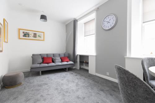 a living room with a couch and a clock on the wall at Lovely City Centre 1 bedroom flat. in Perth