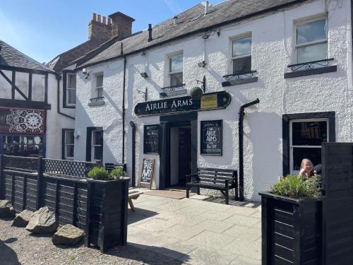 Un uomo seduto fuori da un edificio bianco di Airlie Arms Hotel a Kirriemuir