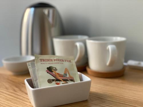 un livre dans un bol sur une table avec des tasses dans l'établissement The Layhead B&B, à Lübeck