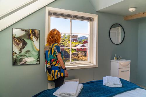 Una mujer parada en un dormitorio mirando por la ventana en Brygga Restaurant and Rooms en Å